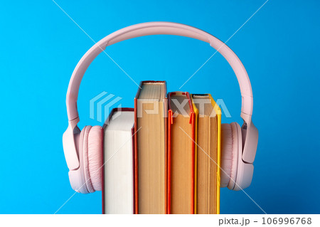 Pink headphones on stack of books against blue background 106996768