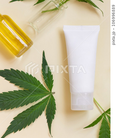 Cream tube near green cannabis leaves top view on beige, CBD cosmetics 106996889