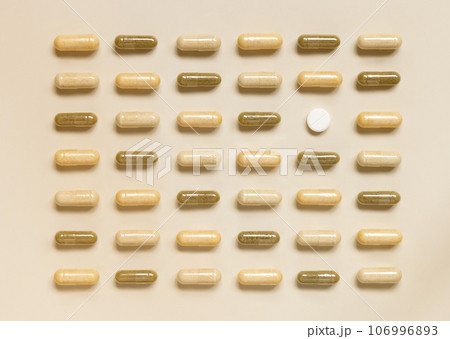 Mix of medical capsules with onewhite pill in lines on light beige top view. Dietary supplements 106996893