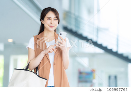 スマホを操作しながらオフィスに通勤するオフィスカジュアルの若い女性 スマホを操作しながらオフィスに通勤するオフィスカジュアルの若い女性 106997765