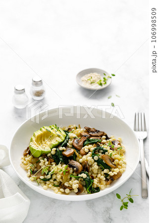 Couscous with avocado, spinach and sauteed champignon mushrooms with onion 106998509