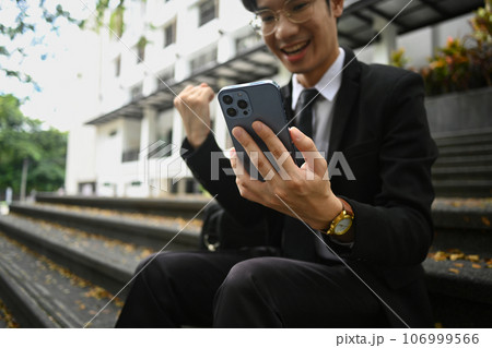 Exited businessman looking at smartphone and celebrating achievement outdoor. Good news, successful, startup Exited businessman looking at smartphone and celebrating achievement outdoor. Good news, successful, startup 106999566