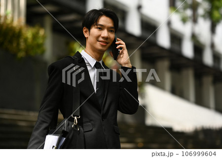 Confident businessman in formal clothes talking on mobile phone while standing in the business district of the city 106999604