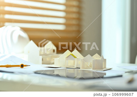 Architectural model of houses on desk with drawing tools and blueprints. Building, construction and architect concept Architectural model of houses on desk with drawing tools and blueprints. Building, construction and architect concept 106999607