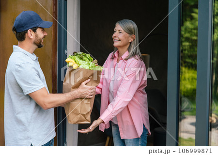 Courier man delivering vegetables to woman at home. Courier man delivering vegetables to woman at home. 106999871