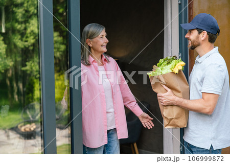Grocery store delivery man delivering food to woman home. Grocery store delivery man delivering food to woman home. 106999872