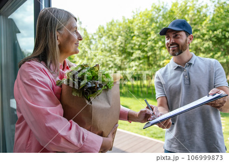 Grocery shopping from the internet-shop, woman client signing some documents with courier. 106999873