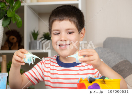 A six-year-old boy plays with slime while sitting at a table at home. A toy for the development of fine motor skills and creativity in children 107000631