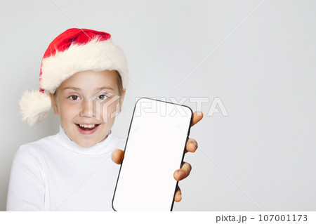 Happy excited Christmas kid Santa showing smartphone with blank empty white screen display Happy excited Christmas kid Santa showing smartphone with blank empty white screen display 107001173