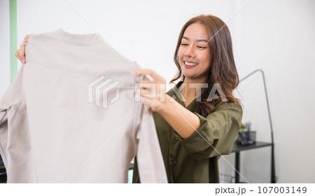 Happy Asian woman customer opening box and looking a new clothes she like it very much, Excited smile female shopper unboxing cardboard box package, shopping online from home, delivery shipping 107003149