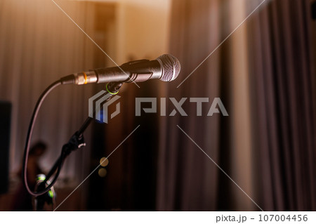 Microphone on stand on stage close up with searchlight light. Professional mic at concert hall or conference room, karaoke, night club, bar. Public events, festival, wedding. Copy space. 107004456
