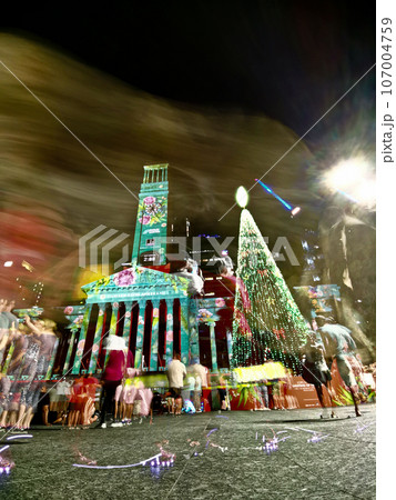Christmas celebration scene at night at Brisbane City Hall. There is a large Christmas tree with light decoration. There are many movement of people in the photo. Christmas celebration scene at night at Brisbane City Hall. There is a large Christmas tree with light decoration. There are many movement of people in the photo. 107004759