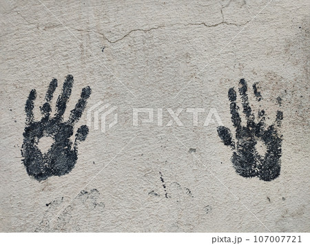 Pair of black prints of children's palms on gray concrete wall, copy space, close-up 107007721