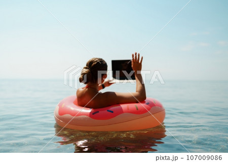 Woman laptop sea. Freelancer woman in sunglases floating on an inflatable big pink donut with a laptop in the sea. People summer vacation rest lifestyle concept Woman laptop sea. Freelancer woman in sunglases floating on an inflatable big pink donut with a laptop in the sea. People summer vacation rest lifestyle concept 107009086