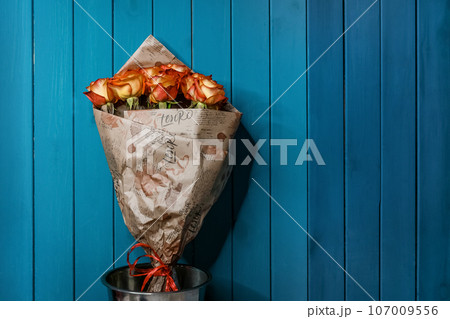 Bouquet of flowers of orange and yellow roses in a decorative paper gift box on a blue wooden background of the interior 107009556