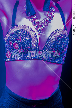 Female sexy body with decorative bust with stones, jewelry and neck jewelry, light erotica, nightlife, club, neon purple blue light 107009557