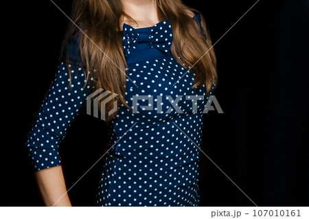 Female skinny figure brunette with long hair in a blue tight-fitting dress with a polka dot pattern on a black background 107010161