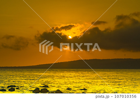 The stunning sunrise view in the Bali Strait, Indonesia, with a foreground of rocky shores along the beach, was captured using the long exposure photography technique. 107010356