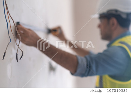 Professional engineer holding tape-line near shabby wall to measure distance before drilling holes skilled specialist in firm uniform prepares places for socket installations 107010385