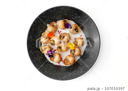 Cooked grape snails in shells on a black plate isolated Cooked grape snails in shells on a black plate isolated 107010397