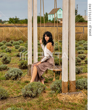 Beautiful young Caucasian woman sitting on a wooden swing. Beautiful young Caucasian woman sitting on a wooden swing. 107011440