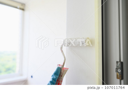 Worker painting on surface wall with paint roller brush. 107011764