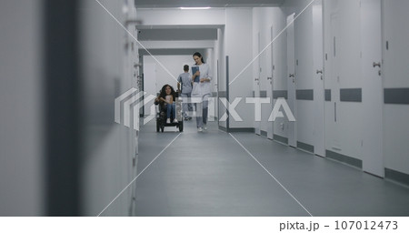 Female doctor walks down the clinic corridor, consults patient with disability 107012473