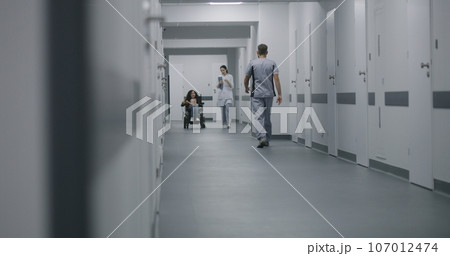 Female doctor walks down the clinic corridor, consults patient with disability 107012474