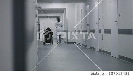 Female doctor walks down the clinic hallway, consults woman with disability 107012481