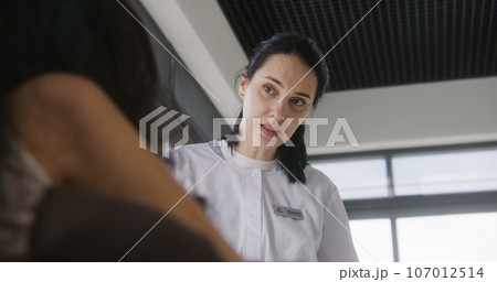 Female doctor consults patient with physical disability in clinic lobby Female doctor consults patient with physical disability in clinic lobby 107012514