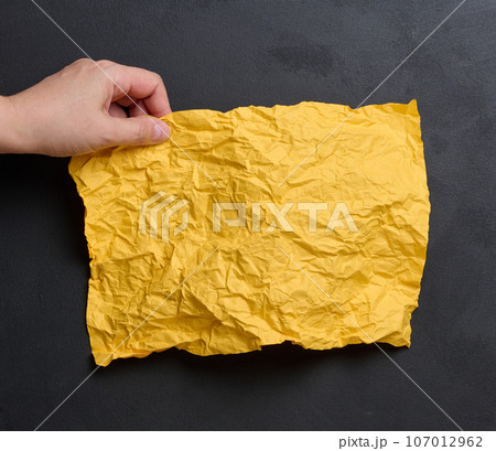 A woman's hand holds a yellow crumpled sheet of paper A woman's hand holds a yellow crumpled sheet of paper 107012962