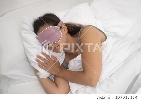 Tranquil lady, sleeping soundly with her sleep mask, lies on a pillow under a warm blanket, exemplifying good sleep practices.  107013154