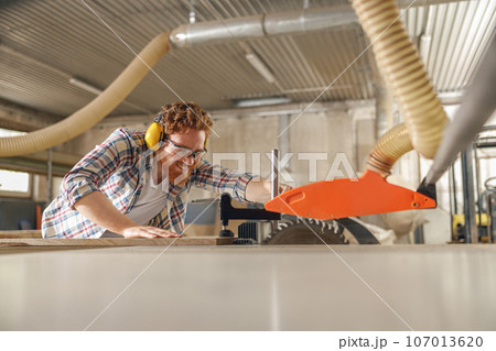 Professional carpenter cutting wooden board at sawmill carpentry manufacturing . Sawing machine Professional carpenter cutting wooden board at sawmill carpentry manufacturing . Sawing machine 107013620
