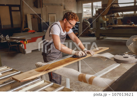 Craftsman coating a wooden board with protective oil in a workshop. Process of making a wood table 107013621