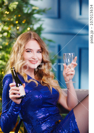 happy attractive woman with bottle and glass of champagne by Christmas tree 107013634