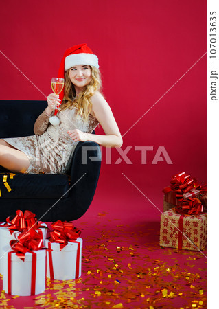 woman in santa hat with champagne and sparklers in red room on sofa with canfeti woman in santa hat with champagne and sparklers in red room on sofa with canfeti 107013635