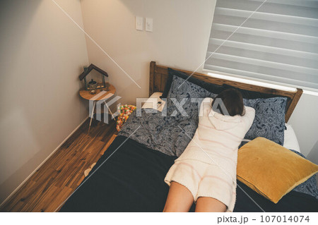 ベットで寝転んでいる若い女性 107014074