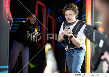 Portrait of positive man with laser gun having fun with her friends on lasertag arena 107015865