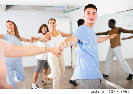Excited young middle-aged men and women couples turning to sides during pair dance practicing in studio for adults Excited young middle-aged men and women couples turning to sides during pair dance practicing in studio for adults 107015967