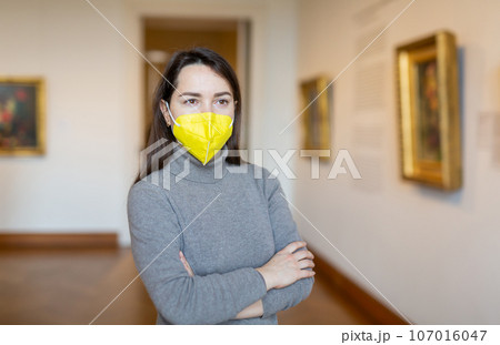 Woman in protective mask viewing collection of paintings in art museum 107016047