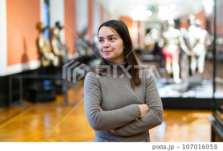 Interested female tourist visiting exhibition of medieval armor in museum 107016058