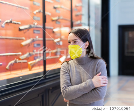 Woman in protective mask examining ancient guns in weapons museum 107016064