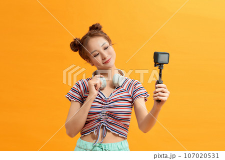 Young woman selfie action cam enjoy over yellow background Young woman selfie action cam enjoy over yellow background 107020531