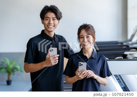 スマホを持つジムのインストラクター スマホを持つジムのインストラクター 107021450