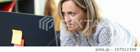 Surprised female manager stands at her working desk and looks at computer screen. 107022309