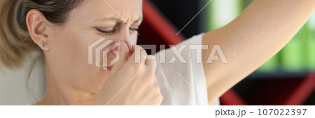 Sad woman closes her nose while looking at her armpit close-up. Sad woman closes her nose while looking at her armpit close-up. 107022397