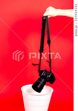 Hand with old digital camera in a trash can, isolated on a red background 107024183