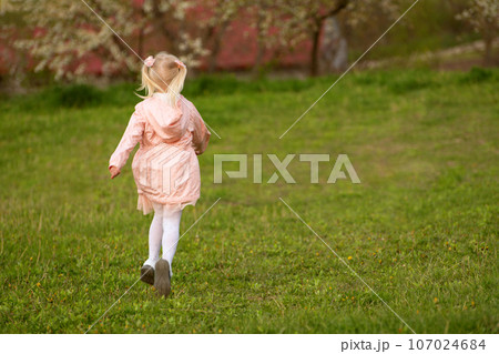 Little European blonde girl with two tails runs through green meadow. Back view. Springtime. Little European blonde girl with two tails runs through green meadow. Back view. Springtime. 107024684