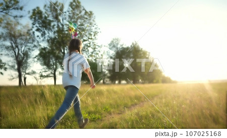 baby pinwheel. little girl silhouette plays with windmill toy wind in the park. happy family childhood dream concept. girl play spinner toy glare of the sun at sunset in a cheerful park fun 107025168