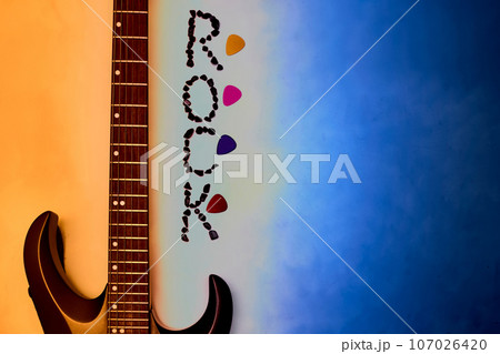 Electric guitar neck, rock inscription, picks on an orange blue gradient 107026420
